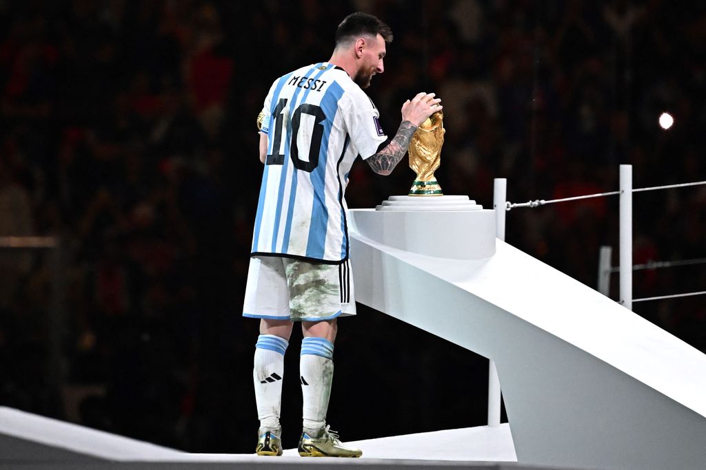 Pemain depan Argentina # 10 Lionel Messi memegang penghargaan Bola Emas untuk pemain terbaik saat ia melihat Trofi Piala Dunia FIFA selama upacara trofi pada akhir pertandingan sepak bola final Piala Dunia Qatar 2022 antara Argentina dan Prancis di Stadion Lusail di Lusail, utara Doha, Qatar, Minggu (18/12/2022).  Argentina menjadi juara Piala Dunia 2022 setelah menang adu penalti atas Prancis 4-2. (Photo by ANNE-CHRISTINE POUJOULAT/AFP via Getty Images)