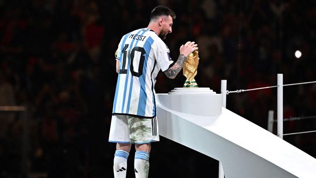 Pemain depan Argentina # 10 Lionel Messi memegang penghargaan Bola Emas untuk pemain terbaik saat ia melihat Trofi Piala Dunia FIFA selama upacara trofi pada akhir pertandingan sepak bola final Piala Dunia Qatar 2022 antara Argentina dan Prancis di Stadion Lusail di Lusail, utara Doha, Qatar, Minggu (18/12/2022).  Argentina menjadi juara Piala Dunia 2022 setelah menang adu penalti atas Prancis 4-2. (Photo by ANNE-CHRISTINE POUJOULAT/AFP via Getty Images)