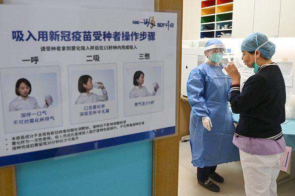A health worker (R) receives a dose of inhalable Covid-19 coronavirus vaccine at a health service center in Chaoyang district in Beijing on November 22, 2022. - China OUT (Photo by CNS / AFP) / China OUT (Photo by -/CNS/AFP via Getty Images)