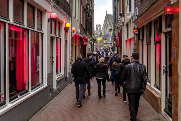 Tourists walking in the red light district of Amsterdam, where prostitutes try to lure customers from behind their window