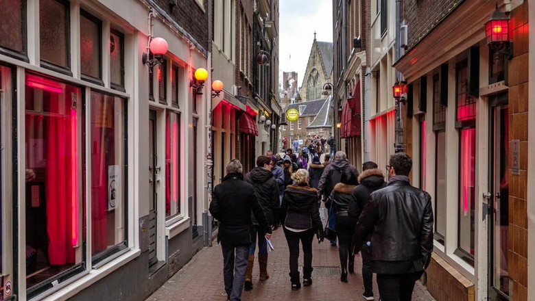 Tourists walking in the red light district of Amsterdam, where prostitutes try to lure customers from behind their window
