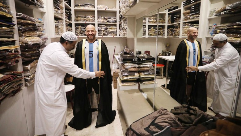 Gegara Messi, Jubah Bisht Jadi Incaran Wisatawan di Qatar DOHA, QATAR - DECEMBER 21: A man tries on a cloak, Bisht, at Souq Waqif Bazaar in Doha, Qatar on December 21, 2022. The traditional Arab world cloak named Bisht, which was dressed by captain of Argentina National Footballl Team Lionel Messi during the award ceremony of the FIFA World Cup 2022 in Qatar, attracts great attention from the fans. (Photo by Ashraf Amra/Anadolu Agency via Getty Images)