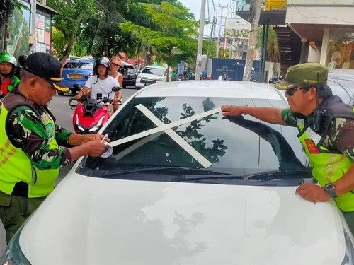 Linmas Tibubeneng memasang tanda silang dengan lakban kertas pada kaca mobil sebagai teguran dilarang parkir sembarangan.