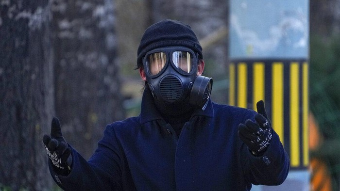 A man wearing a gas mask gestures to a photographer as he walks on a street in Beijing, Tuesday, Dec. 13, 2022. Some Chinese universities say they will allow students to finish the semester from home in hopes of reducing the potential of a bigger COVID-19 outbreak during the January Lunar New Year travel rush. (AP Photo/Andy Wong)