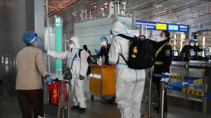 Passengers in protective gear are directed to a flight at a Capital airport terminal in Beijing, Tuesday, Dec. 13, 2022. Some Chinese universities say they will allow students to finish the semester from home in hopes of reducing the potential of a bigger COVID-19 outbreak during the January Lunar New Year travel rush. (AP Photo/Ng Han Guan)