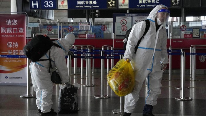 Passengers in protective gear carry their luggage in the Capital airport terminal in Beijing, Tuesday, Dec. 13, 2022. Some Chinese universities say they will allow students to finish the semester from home in hopes of reducing the potential of a bigger COVID-19 outbreak during the January Lunar New Year travel rush. (AP Photo/Ng Han Guan)