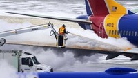 Kru maskapai menyemprotkan cairan khusus untuk membersihkan salju yang menempel di badan pesawat Southwest Airlines. Pembersihan itu dilakukan sebelum pesawat lepas landas, Rabu (21/12/2022). Chris Machian/Omaha World-Herald/AP.