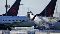 Salju dibersihkan agar tidak mengganggu penerbangan pesawat. Tampak sejumlah kru maskapai membersihkan salju yang menyelimuti pesawat Air Canada di Bandara Internasional Vancouver, Richmond, British Columbia, Rabu (21/12/2022). Darryl Dyck/The Canadian Press/AP.