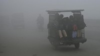 Siswa duduk di atas becak saat dalam perjalanan ke sekolah di tengah cuaca berkabut.  