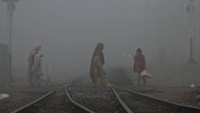 Perempuan melintasi rel kereta api di tengah cuaca berkabut di Lahore. Kabut tebal yang melanda cukup mengganggu aktivitas warga.