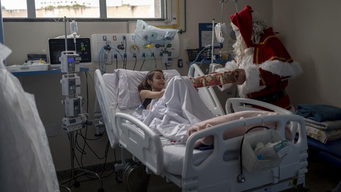 Saat Sinterklas Bawa Harapan di Rumah Sakit Brasil Public worker Ari Queiroz, 59, dressed as Santa Claus, hugs a mother of a patient of the ICU Pediatric ward of the Souza Aguiar Municipal Hospital in Rio de Janeiro, Brazil, on December 22, 2022. - Queiroz, who distributes vaccines and medicines for the Health Department of Rio de Janeiro, has been turning into Santa Claus every Christmas and visiting hospitals for the past two decades. (Photo by MAURO PIMENTEL / AFP) (Photo by MAURO PIMENTEL/AFP via Getty Images)