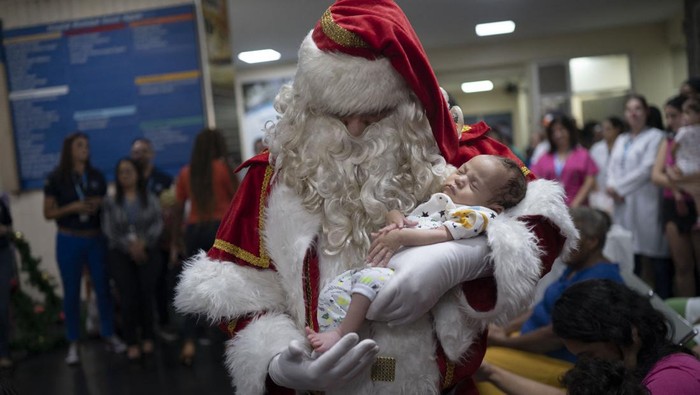 Public worker Ari Queiroz, 59, dressed as Santa Claus, hugs a mother of a patient of the ICU Pediatric ward of the Souza Aguiar Municipal Hospital in Rio de Janeiro, Brazil, on December 22, 2022. - Queiroz, who distributes vaccines and medicines for the Health Department of Rio de Janeiro, has been turning into Santa Claus every Christmas and visiting hospitals for the past two decades. (Photo by MAURO PIMENTEL / AFP) (Photo by MAURO PIMENTEL/AFP via Getty Images)