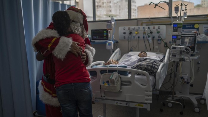 Public worker Ari Queiroz, 59, dressed as Santa Claus, hugs a mother of a patient of the ICU Pediatric ward of the Souza Aguiar Municipal Hospital in Rio de Janeiro, Brazil, on December 22, 2022. - Queiroz, who distributes vaccines and medicines for the Health Department of Rio de Janeiro, has been turning into Santa Claus every Christmas and visiting hospitals for the past two decades. (Photo by MAURO PIMENTEL / AFP) (Photo by MAURO PIMENTEL/AFP via Getty Images)