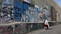 Seorang pria mengenakan pakaian Sinterklas berjalan di sepanjang tembok pemisah wilayah Israel di kota Bethlehem, Tepi Barat.