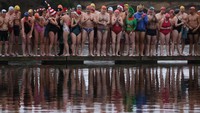 Sejumlah peserta berbaris di pinggir kolam untuk mengikuti perlombaan renang saat hari Natal di London, Inggris, Minggu (25/12/2022).