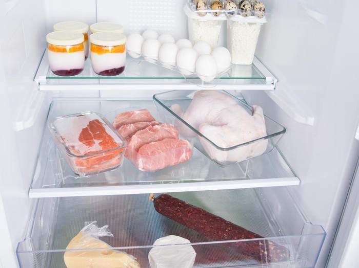 in the open refrigerator, on glass shelves, there are products, whole chicken, meat, eggs, cheese, sausage, cottage cheese and yogurt
