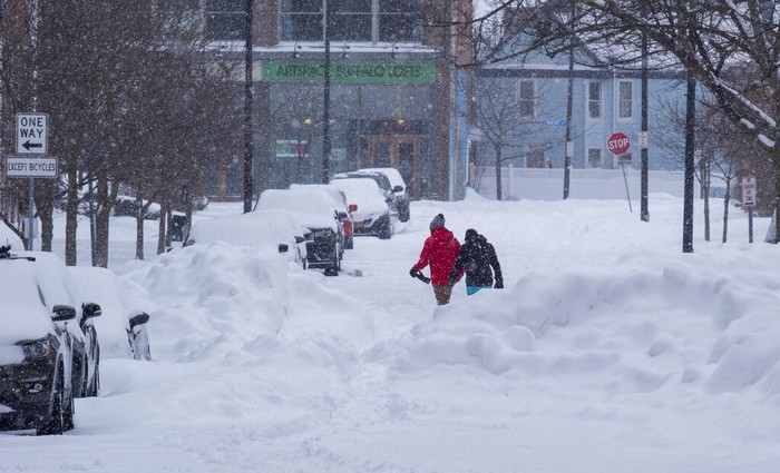 People move about the streets of the Elmwood Village neighborhood of Buffalo, N.Y. Monday, Dec. 26, 2022, after a massive snow storm blanketed the city. Along with drifts and travel bans, many streets were impassible due to abandoned vehicles. (AP Photo/Craig Ruttle)