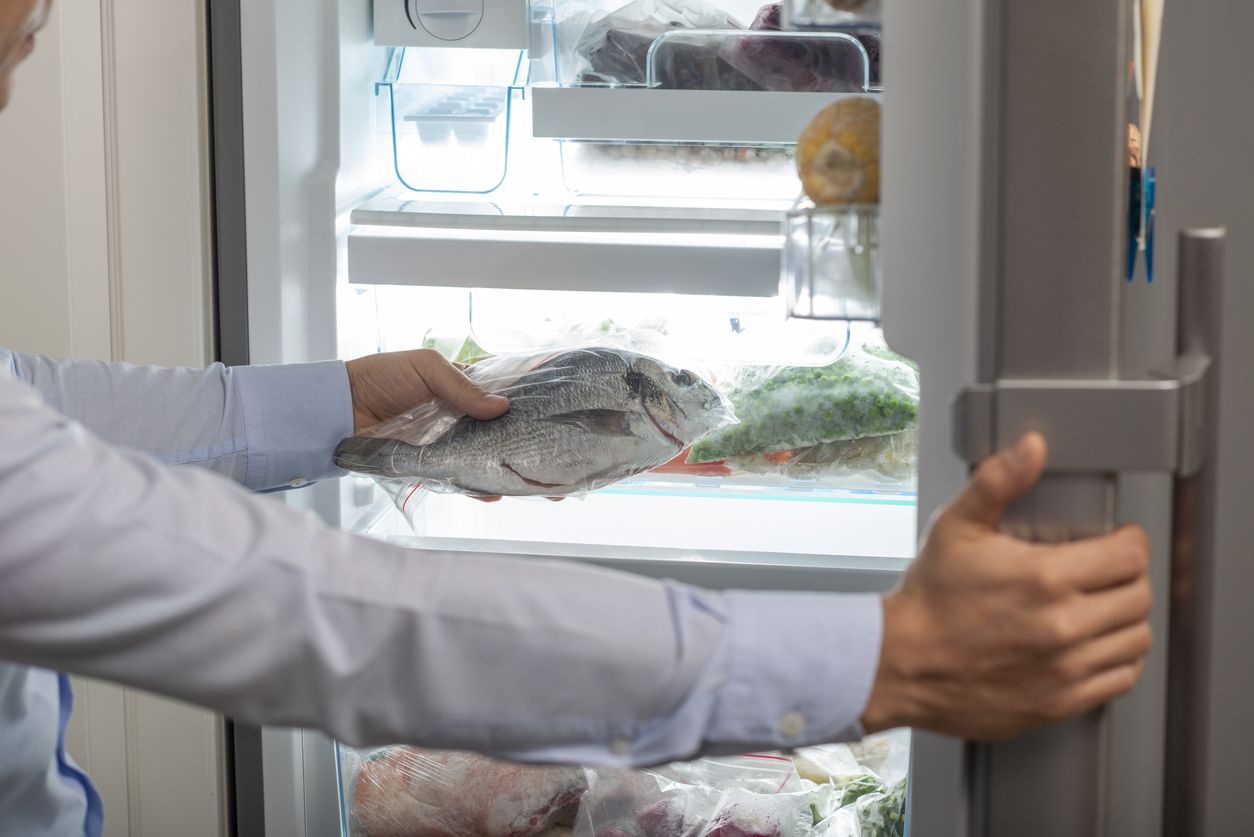 A man taking a fish into fridge.