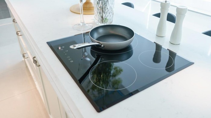 Frying pan on modern black induction stove, cooker, hob or built in cooktop with ceramic top in white kitchen interior