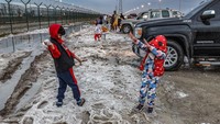 Dua orang anak nampak gembira bermain es di pinggir jalan.  