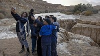 Orang-orang berswafoto dengan latar belakang gurun Negev yang tengah dilanda banjir bandang.  