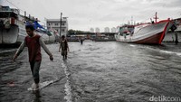 Nelayan melintasi banjir rob saat cuaca buruk di Pelabuhan Muara Baru, Penjaringan, Jakarta Utara, Rabu (28/12/2022).