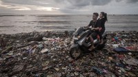 Pengendara roda dua melintasi tumpukan sampah yang terbawa gelombang air laut di Labuan, Pandeglang, Banten, Selasa (27/12/2022).