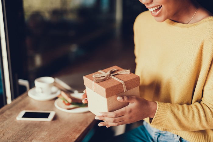 Cropped photo of charming exited lady in cafe. She holding brown box with present and smiling