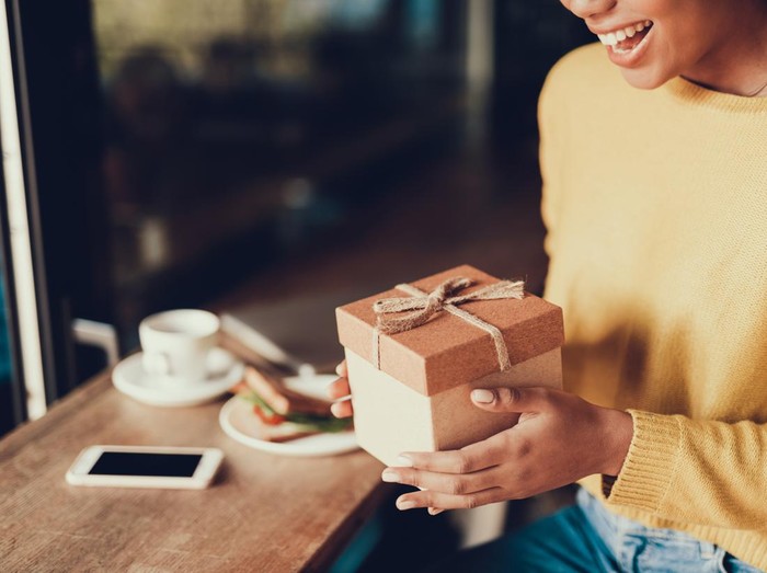 Cropped photo of charming exited lady in cafe. She holding brown box with present and smiling