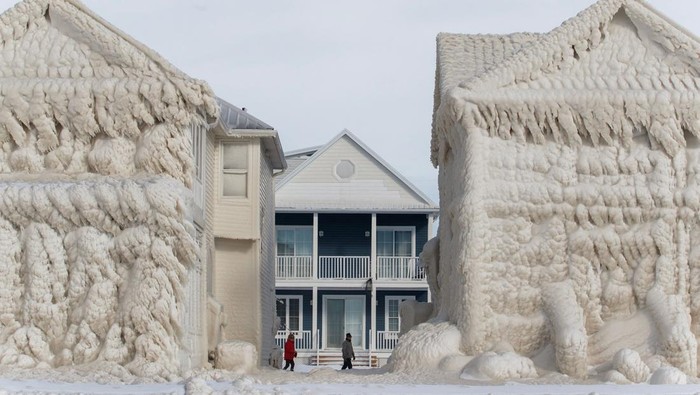 People walk by homes covered in ice at the waterfront community of Crystal Beach in Fort Erie, Ontario, Canada, on December 28, 2022, following a massive snow storm that knocked out power in the area to thousands of residents. (Photo by Cole Burston / AFP) (Photo by COLE BURSTON/AFP via Getty Images)