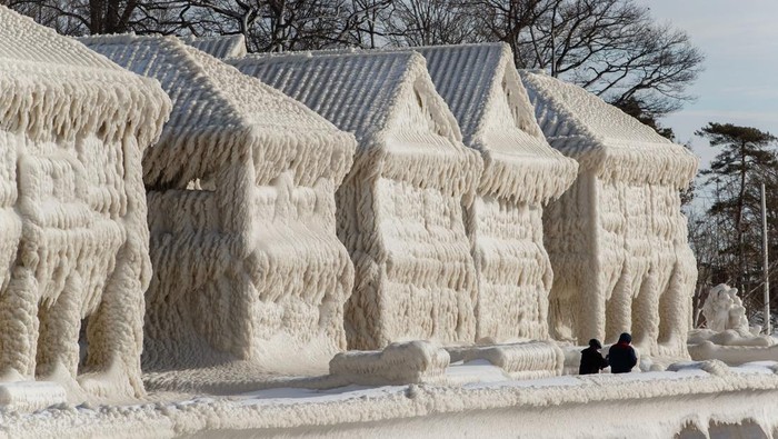 People walk by homes covered in ice at the waterfront community of Crystal Beach in Fort Erie, Ontario, Canada, on December 28, 2022, following a massive snow storm that knocked out power in the area to thousands of residents. (Photo by Cole Burston / AFP) (Photo by COLE BURSTON/AFP via Getty Images)