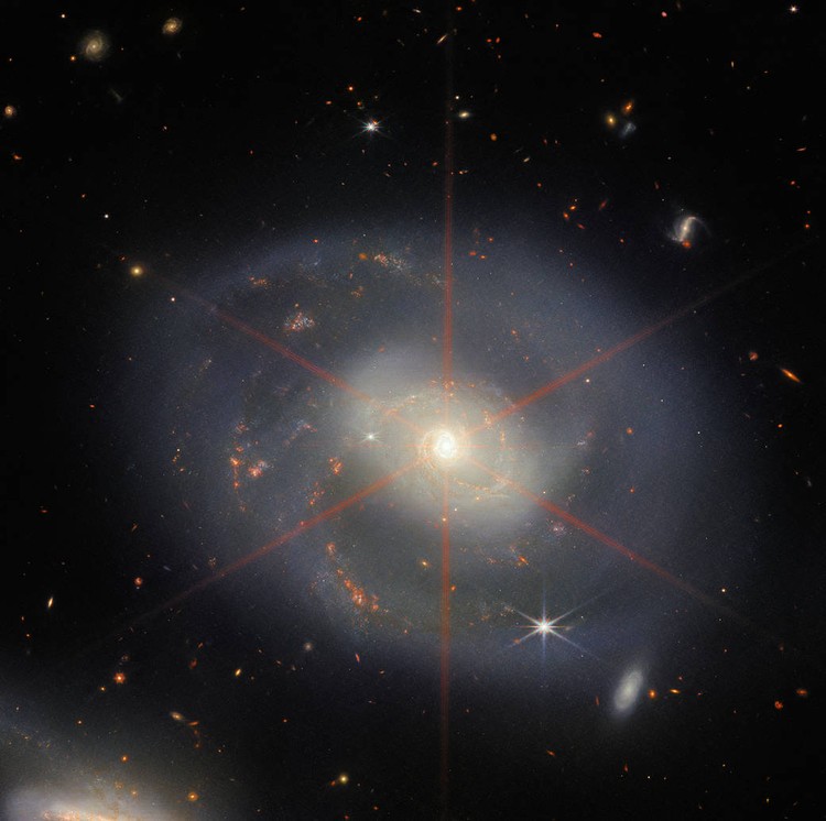 James Webb This image is dominated by NGC 7469, a luminous, face-on spiral galaxy approximately 90 000 light-years in diameter that lies roughly 220 million light-years from Earth in the constellation Pegasus. Its companion galaxy IC 5283 is partly visible in the lower left portion of this image. This spiral galaxy has recently been studied as part of the Great Observatories All-sky LIRGs Survey (GOALS) Early Release Science program with the NASA/ESA/CSA James Webb Space Telescope, which aims to study the physics of star formation, black hole growth, and feedback in four nearby, merging luminous infrared galaxies. Other galaxies studied as part of the survey include previous ESA/Webb Pictures of the Month II ZW 096 and IC 1623. NGC 7469 is home to an active galactic nucleus (AGN), which is an extremely bright central region that is dominated by the light emitted by dust and gas as it falls into the galaxys central black hole. This galaxy provides astronomers with the unique opportunity to study the relationship between AGNs and starburst activity because this particular object hosts an AGN that is surrounded by a starburst ring at a distance of a mere 1500 light-years. While NGC 7469 is one of the best studied AGNs in the sky, the compact nature of this system and the presence of a great deal of dust have made it difficult for scientists to achieve both the resolution and sensitivity needed to study this relationship in the infrared. Now, with Webb, astronomers can explore the galaxys starburst ring, the central AGN, and the gas and dust in between. Using Webbs MIRI, NIRCam and NIRspec instruments to obtain images and spectra of NGC 7469 in unprecedented detail, the GOALS team has uncovered a number of details about the object. This includes very young star-forming clusters never seen before, as well as pockets of very warm, turbulent molecular gas, and direct evidence for the destruction of small dust grains within a few hundred light-years of the nucleus proving
