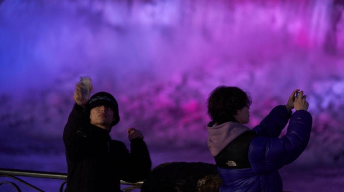 Keindahan Air Terjun di Kanada Saat Berpendar Cahaya Warna-warni Tourists takes a selfie at the Horseshoe Falls in Niagara Falls, Ontario, on December 28, 2022. - Niagara Falls only saw a small amount of snow during the winter storm which hit the region late last week but Buffalo, only 40km away received an epic blast of lake effect snow. (Photo by Geoff Robins / AFP) (Photo by GEOFF ROBINS/AFP via Getty Images)