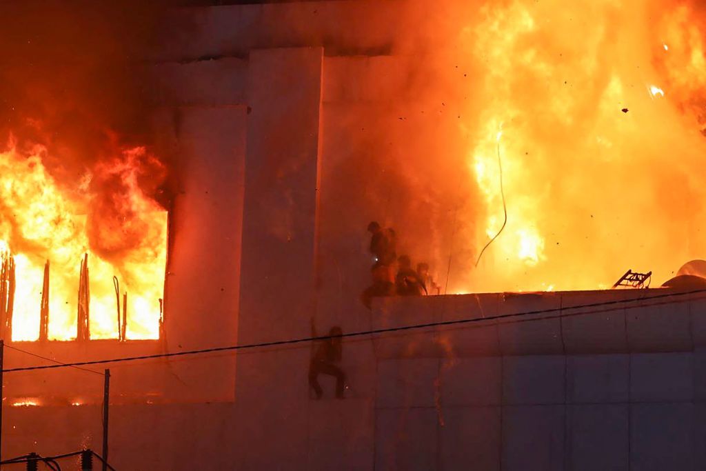 TOPSHOT - Fire burns around people on a ledge on the side of the Grand Diamond City hotel-casino in Poipet on December 29, 2022. - As many as 10 people have died in a fire at a Cambodian hotel-casino on the border of Thailand, with photos showing groups desperately huddled on ledges as fierce flames surround them. (Photo by AFP) (Photo by STR/AFP via Getty Images)