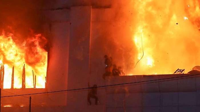 TOPSHOT - Fire burns around people on a ledge on the side of the Grand Diamond City hotel-casino in Poipet on December 29, 2022. - As many as 10 people have died in a fire at a Cambodian hotel-casino on the border of Thailand, with photos showing groups desperately huddled on ledges as fierce flames surround them. (Photo by AFP) (Photo by STR/AFP via Getty Images)