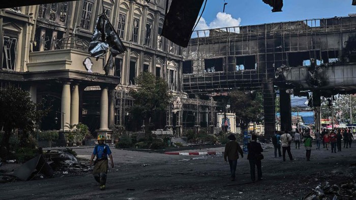 People walk under a destroyed part of the Grand Diamond City hotel-casino after a fire in Poipet on December 29, 2022. - About 10 people are dead and more than a dozen on life support after a fire at a Cambodian border casino, with photos from the scene showing people desperately huddled on ledges and perched on windowsills in a bid to escape the flames. (Photo by Lillian SUWANRUMPHA / AFP) (Photo by LILLIAN SUWANRUMPHA/AFP via Getty Images)