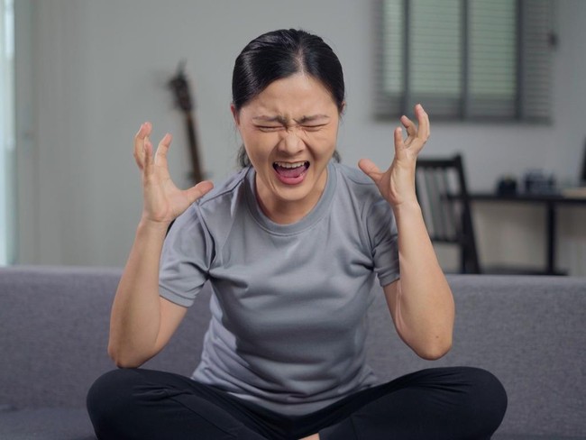Asian woman angry seriously sitting on sofa in living room at home looking at camera and shouting.