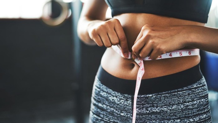Cropped shot of a fit young woman measuring her waist in a gym