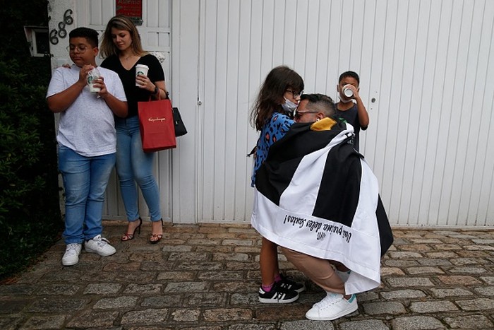 A fan of Brazilian football legend Pele wrapped in a flag of Brazilian team Santos, embraces a girl in front of the Albert Einstein Israelite Hospital, where Pele died after a long battle with cancer, in Sao Paulo, Brazil, on December 29, 2022. - Brazilian football icon Pele, widely regarded as the greatest player of all time and a three-time World Cup winner who masterminded the 