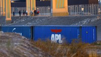 Migran pencari suaka berjalan melewati pagar dekat peti kemas yang ditempatkan di El Paso, Texas, di tepi sungai Rio Bravo, perbatasan antara AS dan Meksiko.