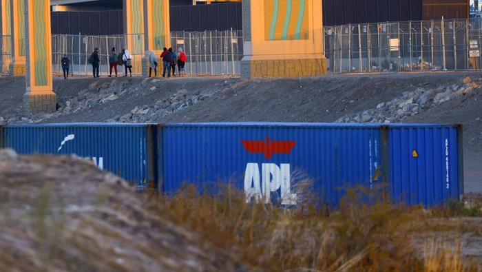 Asylum-seeking migrants walk past a fence near containers that were placed in El Paso, Texas, on the banks of the Rio Bravo river, the border between the U.S. and Mexico, with the purpose of reinforcing border security and inhibiting the crossing of migrants into the U.S., seen from Ciudad Juarez, Mexico, December 29, 2022. REUTERS/Jose Luis Gonzalez