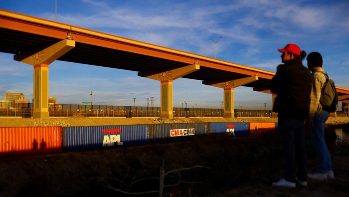 Asylum-seeking migrants walk past a fence near containers that were placed in El Paso, Texas, on the banks of the Rio Bravo river, the border between the U.S. and Mexico, with the purpose of reinforcing border security and inhibiting the crossing of migrants into the U.S., seen from Ciudad Juarez, Mexico, December 29, 2022. REUTERS/Jose Luis Gonzalez