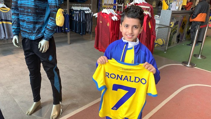 A young fan holds t-shirt bearing the name Ronaldo and number 7, at the Saudi Al Nassr FC shop in the Saudi capital Riyadh, on December 31, 2022. - Cristiano Ronaldo on December 30 signed for Al Nassr of Saudi Arabia, the club announced, in a deal believed to be worth more than 200 million euros. The 37-year-old penned a contract which will take him to June 2025. (Photo by Fayez Nureldine / AFP) (Photo by FAYEZ NURELDINE/AFP via Getty Images)