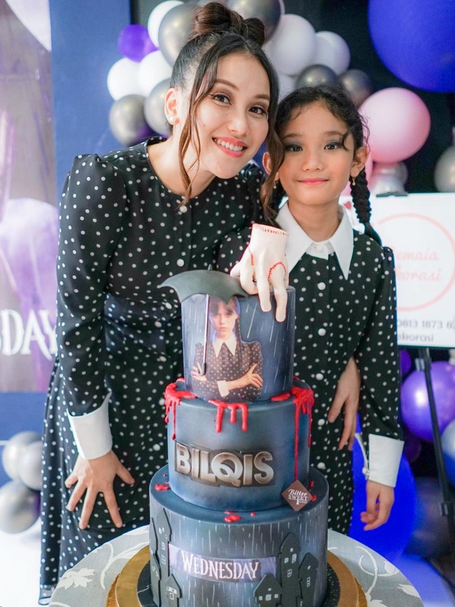 Sesuai dengan tema, dekorasi di perayaan ulang tahun Bilqis didominasi oleh warna ungu dan abu-abu. Kue ulang tahunnya pun unik dibuat 3 susun dengan potret pemeran Wednesday Addams di bagian atasnya. Foto: Instagram/@ayutingting92