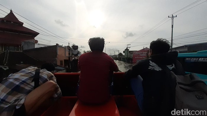 Surya (40) dan beberapa warga lain melintasi banjir Jalan Kaligawe Semarang menaiki truk, Senin (2/1/2023).