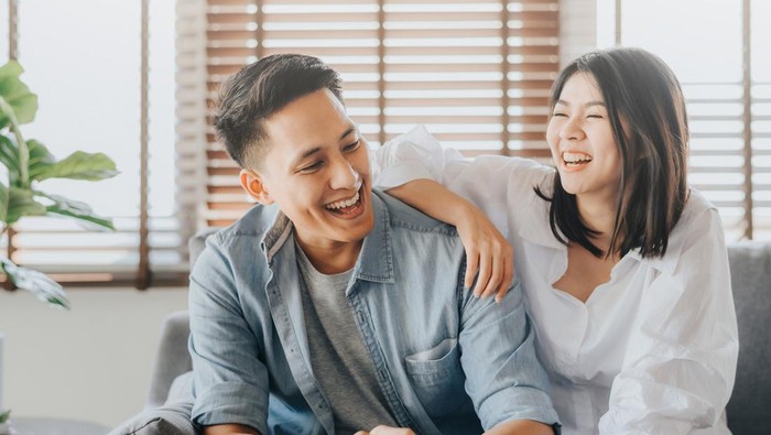 Happy Asian couple having fun and laughing together in living room at home