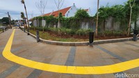 Terdapat lampu taman di sisi trotoar dengan tembok lawas yang ditumbuhi tanaman merambat.