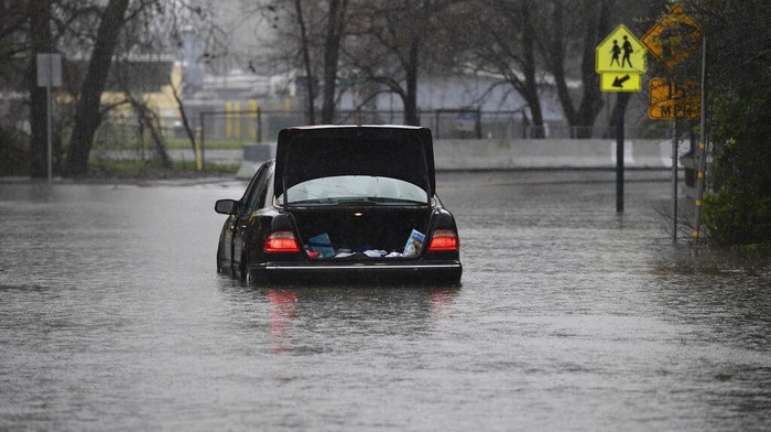 Badai Dahsyat Terjang AS Sebabkan Banjir hingga Longsor Patsy Costello, 88, waits in her vehicle for over an hour on Astrid Drive in Pleasant Hill, Calif., on Saturday, Dec. 31, 2022. Costello drove her car on the flooded street thinking she could make it when it stalled in the two feet of water. After two hours the water had receded about a foot making it easier to rescue her. Police were called but stood by and watched after calling in a tow truck to help pull the car out of the water. Nurse Katie Leonard, of Pleasant Hill, lives down the block used her kayak to bring Costello hot tea, blankets, food and a phone to call a friend. (Jose Carlos Fajardo/Bay Area News Group via AP)