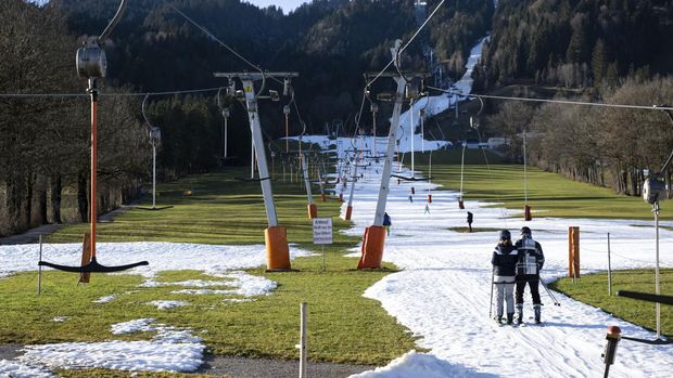 People ski up the slope on the Draxlhang in the Brauneck ski area using a T-bar lift in Lenggries, Germany, Wednesday, Dec. 28, 2022. Sparse snowfall and unseasonably warm weather in much of Europe is allowing green grass to blanket many mountaintops across the region where snow might normally be. It has caused headaches for ski slope operators and aficionados of Alpine white this time of year. (Sven Hoppe/dpa via AP)