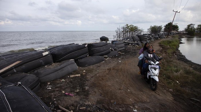 Villagers ride motorbikes past giant sandbags to resist abrasion from sea waves in Cemarajaya village, Karawang regency, West Java province, on December 6, 2022. According to villagers, the rate of abrasion due to waves and sea level rise in Cemarajaya village is fast, with an average of 5 meters of land sinking each year.  Since 2000, waves and rising sea levels accompanied by tidal floods have begun to hit the village after the plantation land was converted into a shrimp pond.  Now, the village, which was originally about 500 meters from the shoreline, has become the front line that was hit by waves, and is still experiencing abrasion that threatens the village's existence. (Photo by Aditya Irawan/NurPhoto via Getty Images)